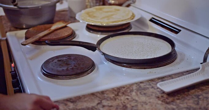 A delicious crepe cooks on a hot pan atop an electric stove, its surface bubbling as it heats. A stack of freshly prepared pancakes waits nearby, promising a comforting homemade breakfast.