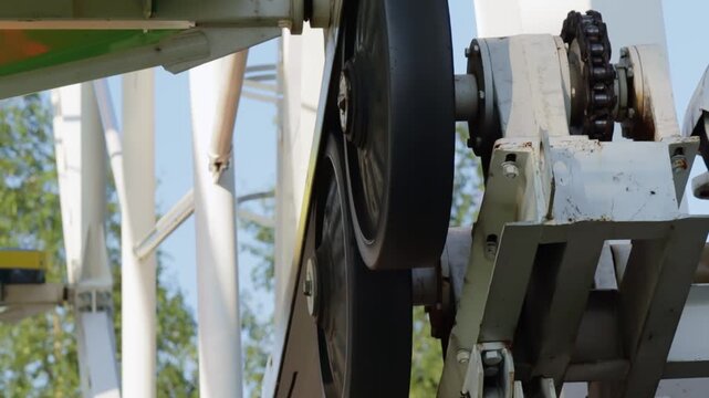 Detailed view of the Ferris wheel's drive system, showcasing a large wheel engaged with a chain mechanism. The vibrant blue and yellow cabin section adds a pop of color against the industrial metal co