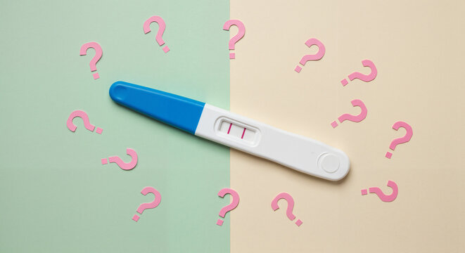 Pregnancy test with question marks on pastel background  