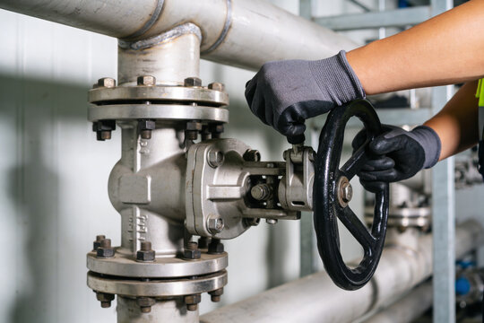 Industrial worker in gloves turning a large valve on a complex pipe system