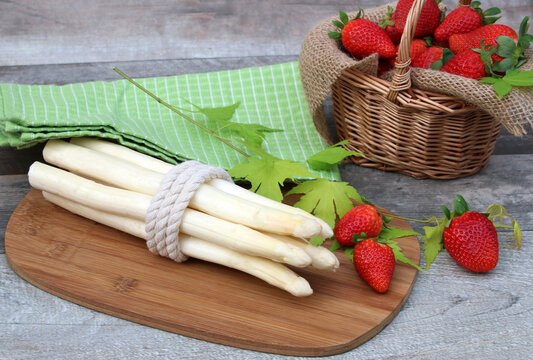 Fresh white asparagus tied together with strawberries on a rustic wooden board.
