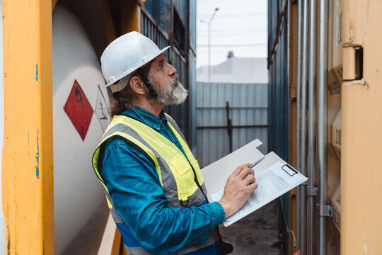 Senior industrial safety inspector pointing at hazardous caution label on cargo container. Logistics manager using tablet for compliance checking.