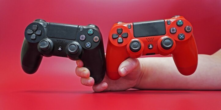 Two DualShock 4 gamepads in his hands on a red background. Black and red controllers, front view, studio shooting.