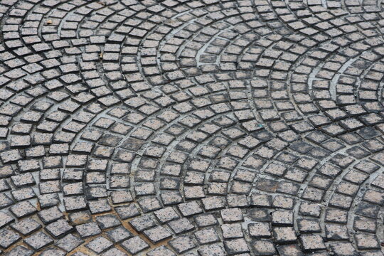 Curved stone pavers form elegant arches. Gray grout lines define each tile's shape. Weathered texture suggests age and use. Pattern repeats in graceful, circular flow