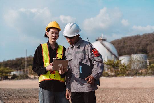 Industrial engineer and safety inspector reviewing project on clipboard. Male and female workers discussing equipment maintenance and quality control at site.