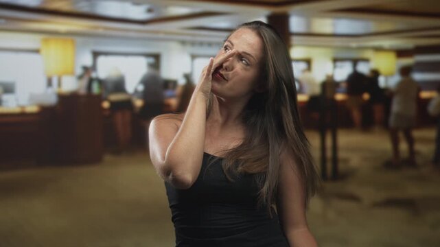 Young brunette woman in black tanktop touching nose with hand, rubbing face and closing eyes in a building lobby; fatigue reflection.