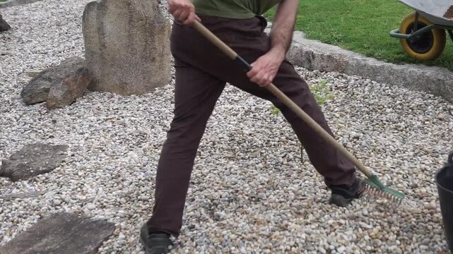 Close-up of a landscaper using a rake to level small pebbles in a Zen-style garden, focusing on detail-oriented outdoor design.