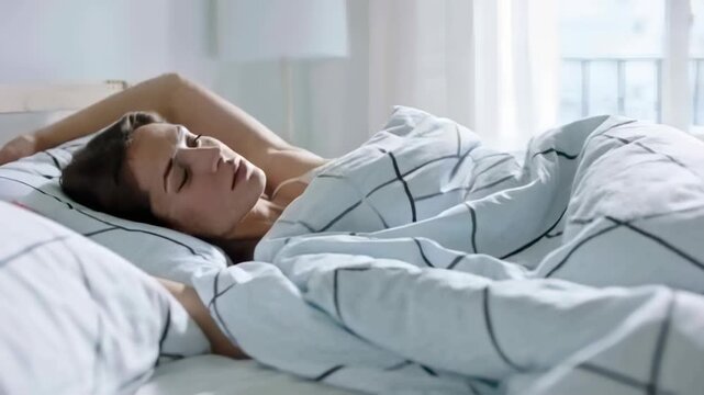 Waking woman in cami opening eyes reaching duvet raising arms settling as dawn light filling room