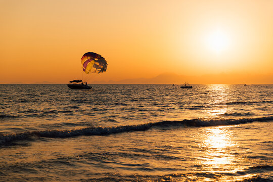 Boat towing colorful parasail over ocean during golden sunset.