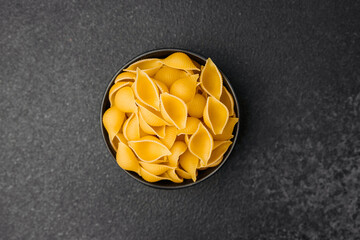 Fototapeta premium Different shapes of uncooked pasta arranged in a bowl on a dark surface