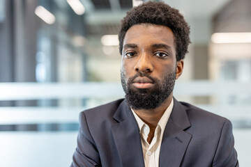 Naklejka premium Young businessman with ethnic background and beard standing directly to camera, showing confidence and professionalism in a contemporary corporate environment