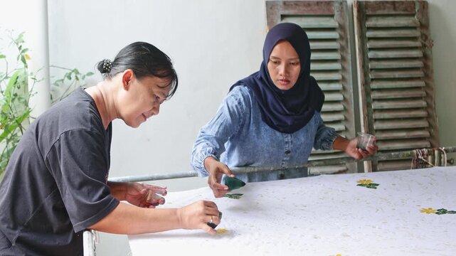 Two Indonesian women crafting traditional handmade batik fabric