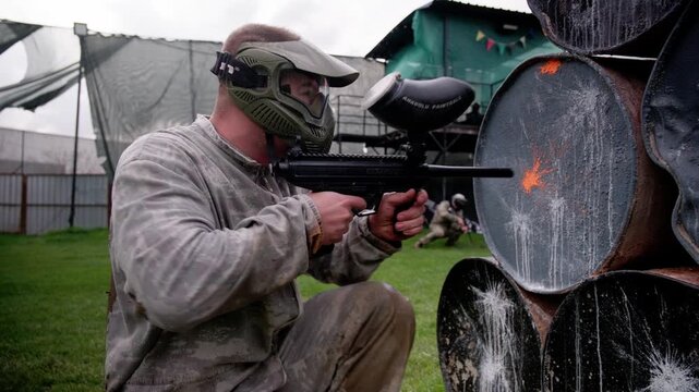 Side View of Paintball Player Shooting Behind Cover in Combat Scene
