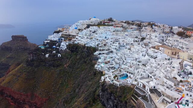 Aerial video of Imerovigli, Santorini, showing the whitewashed boutique hotels and traditional churches perched on the highest point of the caldera rim under a moody sky.