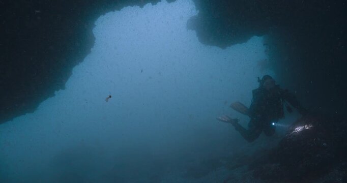 Scuba diver holds on to rock at entrance to cave in low visibility.