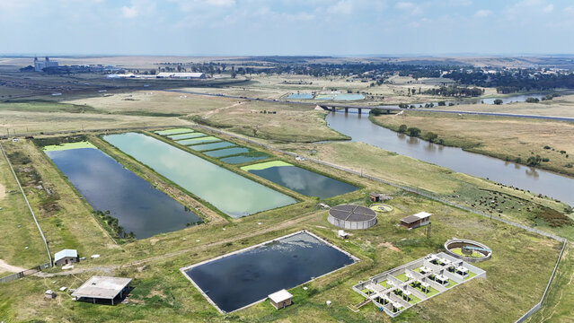 Aerial view of the Vaal River flowing past a water treatment facility with settling ponds and green fields in Villiers, Free State, South Africa.