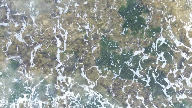 Aerial View of Foamy Ocean Waves Breaking on Rocky Coast