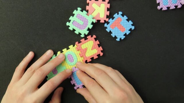 Closeup of child's hands playing with a eva foam letters puzzle. Child's hands playing with an educational toy. Kid's hands building blocks.