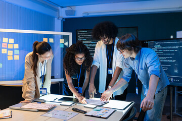 Fototapeta premium Diverse group of technical experts analyzing creative sketches on table in office. Young professional team collaborating on software development and project planning during meeting