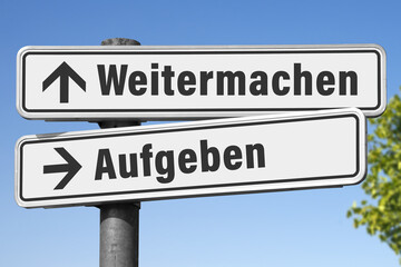 Ein symbolisches Wegweiser-Schild, das die gegensätzlichen Entscheidungen „Weitermachen“ und...