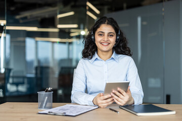 Fototapeta premium Young businesswoman with a headset and tablet assisting customers, providing help and support for telemarketing or call center services in a modern office setup