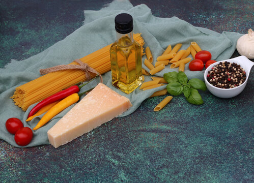 Pasta ingredients: spaghetti, penne, parmesan, garlic, basil, colorful chili peppers and cherry tomatoes on a green stone base.
