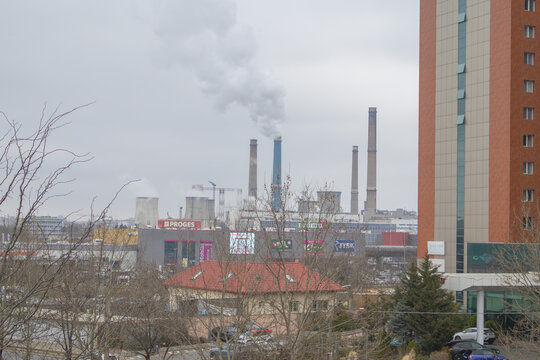 Urban landscape in Bucharest featuring smoking industrial chimneys of CET Sud power station towering over commercial buildings and a modern residential high-rise - Bucuresti, Romania - March 15 2026