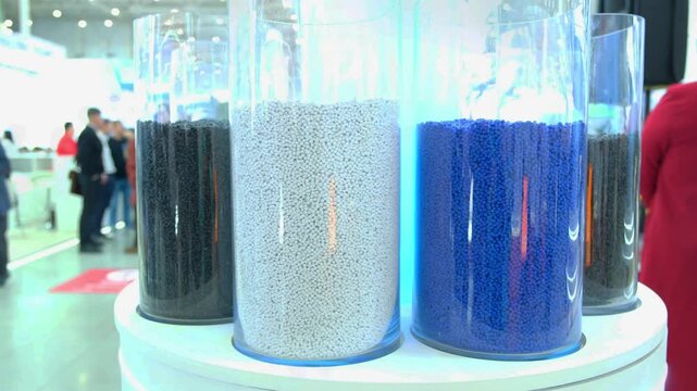 Moscow. Russia, 11.03.2026 Colored plastic polymer pellets stored in clear cylindrical containers at industrial exhibition. Raw material for manufacturing industry, chemical industry concept.