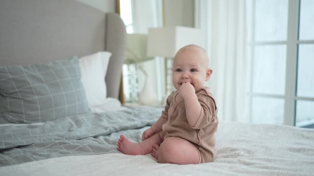 Happy baby. Cute little newborn girl with smiling face sitting on bed in bedroom. Infant baby resting playing crawling on blanket at home. Motherhood happy child childcare concept