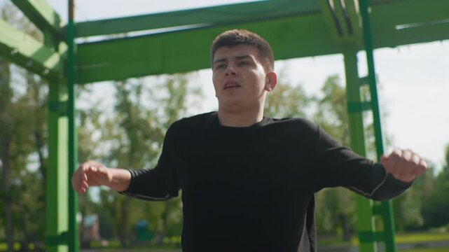 Calm breathing exercise, Relaxed individual practicing mindful stretching outdoors, Young person performs slow breathing and stretching routines beneath metal arbor in tranquil park setting
