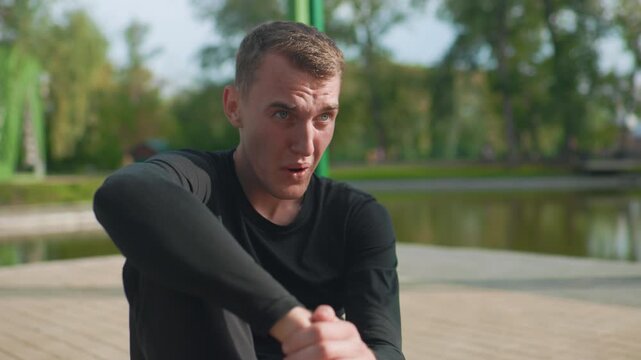 white man struggling with fatigue post run, seated on dock beside pond, shielding eyes from sun, heavy breathing, wet hair, black compression top, green columns and trees in background, determination