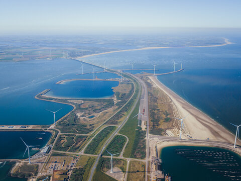 Aerial view of the Eastern Scheldt Storm Surge Barrier with wind turbines along the coast and blue water in Vrouwenpolder, Zeeland, Netherlands.
