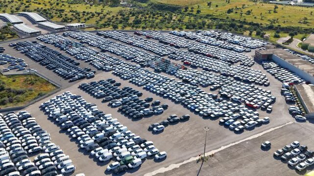 Cinematic forward drone shot over a massive automotive storage terminal. Thousands of new cars parked in neat rows highlight global supply chain and industrial logistics.