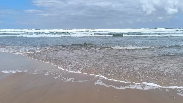 Cinematic footage of restless ocean waves rolling and crashing onto a sandy beach under bright sunlight.