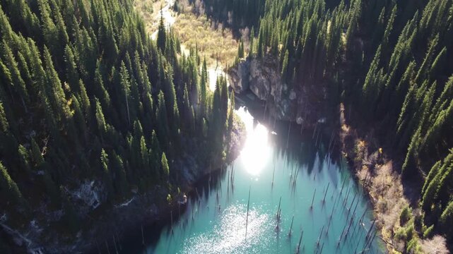 High angle view of turquoise Kaindy lake with submerged trees and bright sun reflection, mystical forest, Kazakhstan. High quality 4k footage