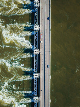 Aerial view of the Eastern Scheldt Storm Surge Barrier with turbulent water rushing through open gates and cars on the road in Vrouwenpolder, Zeeland, Netherlands.