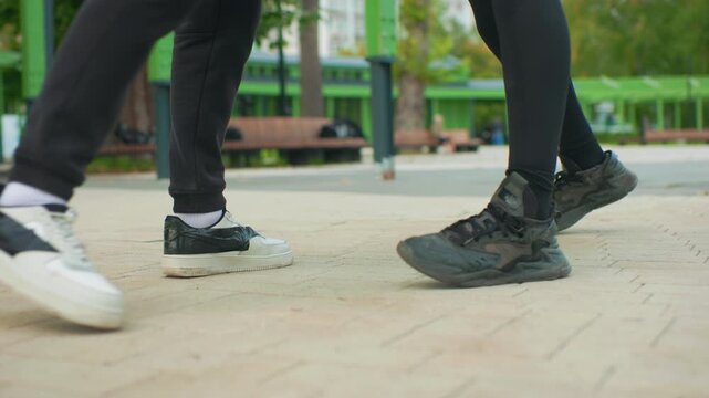 park closeup feet synchronized rhythm play, two performers rehearsing duet steps on tiled plaza with matching sneakers, gentle connection through mirrored footwork, calm outdoor mood and precise