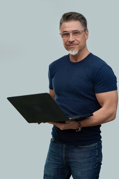 Casual mid adult man standing holding laptop computer. Portrait of happy middle aged male in 50s with gray hair and glasses, smiling. Isolated on white background.