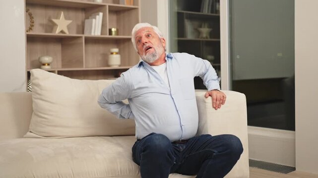Backache back pain. Unhappy senior old man suffering from backache at home. Upset elder man feel sudden back pain muscles ache tension injury. Sad grandfather feeling pain hurt in back touching spine