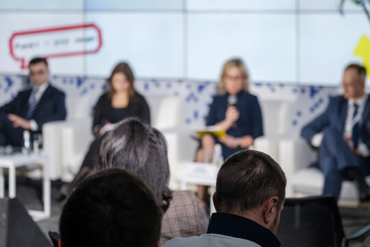 Audience watches panel discussion at corporate conference, speakers on stage, professional networking and business presentation.