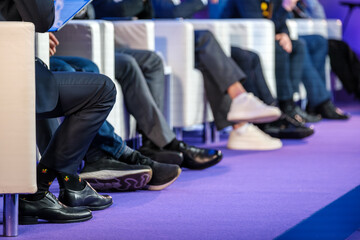Obraz premium Business conference panel captured from low angle, focus on legs and footwear, formal and casual mix, vibrant purple stage.