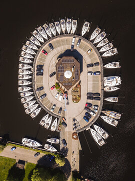 Aerial view of a circular marina with sailboats docked in a radial pattern around a central building and parking lot in Lemmer, Friesland, Netherlands.