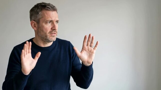 Middle-aged man saying no and making a stop gesture with his hands. Serious Caucasian male showing refusal and disagreement against a grey background. Copy space for text