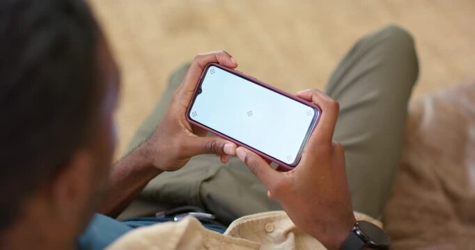 Adult man is holding phone horizontally on couch while loading icon is making thumbs shift