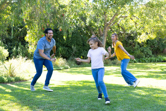 Diverse family playing and chasing child running across mowed lawn in park with sneakers