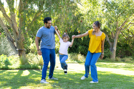 Diverse family lifting child between parents on lawn in jeans and sneakers showing orthopedic boot
