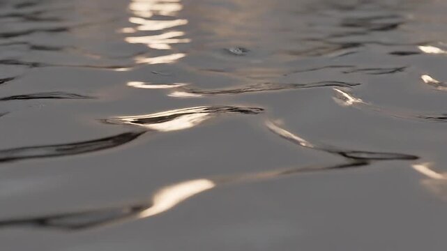Close-up perspective of a dark water surface with dynamic ripples and bright golden light reflections creating an abstract and energetic background texture Keywords: water, surface, ripples, waves