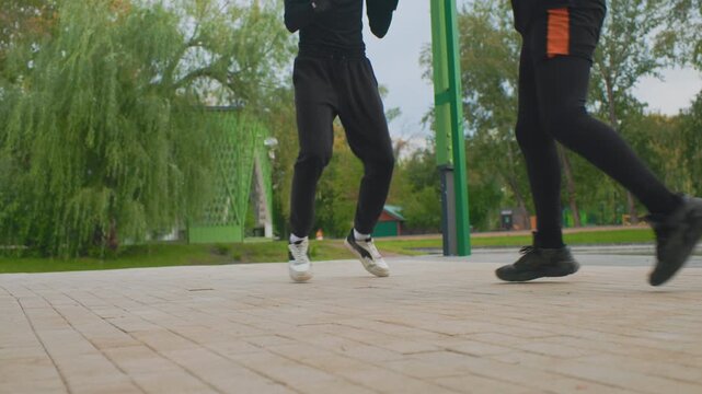 park plaza dynamic footwork training session with synchronized steps and pivots, two athletes in leggings and mixed sneakers rehearse drills and slides on paved promenade, focused coachlike
