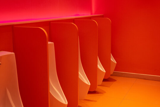 Red public bathroom with rows of urinals