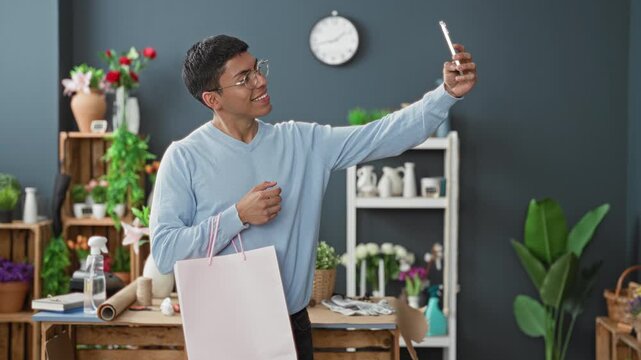 Man holding pink shopping bag and tapping smartphone with both hands inside building florist shop, smiling slightly; everyday connection contentment.